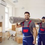 Smiling,Young,Male,Movers,Carrying,Carpet,Unload,Goods,In,Client